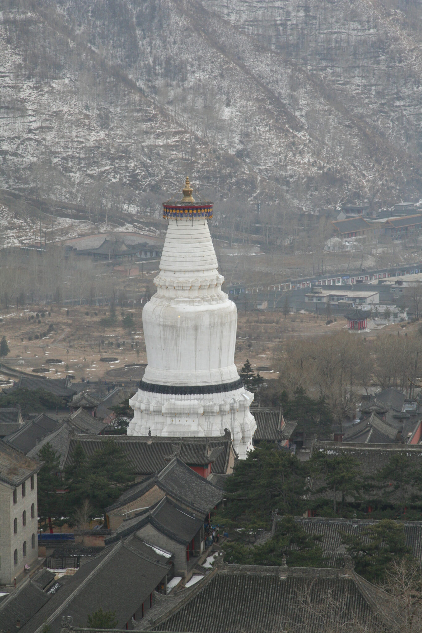 Monumental white stupa stands in sharp contrast to surrounding low-slung buildings and mountain in background
