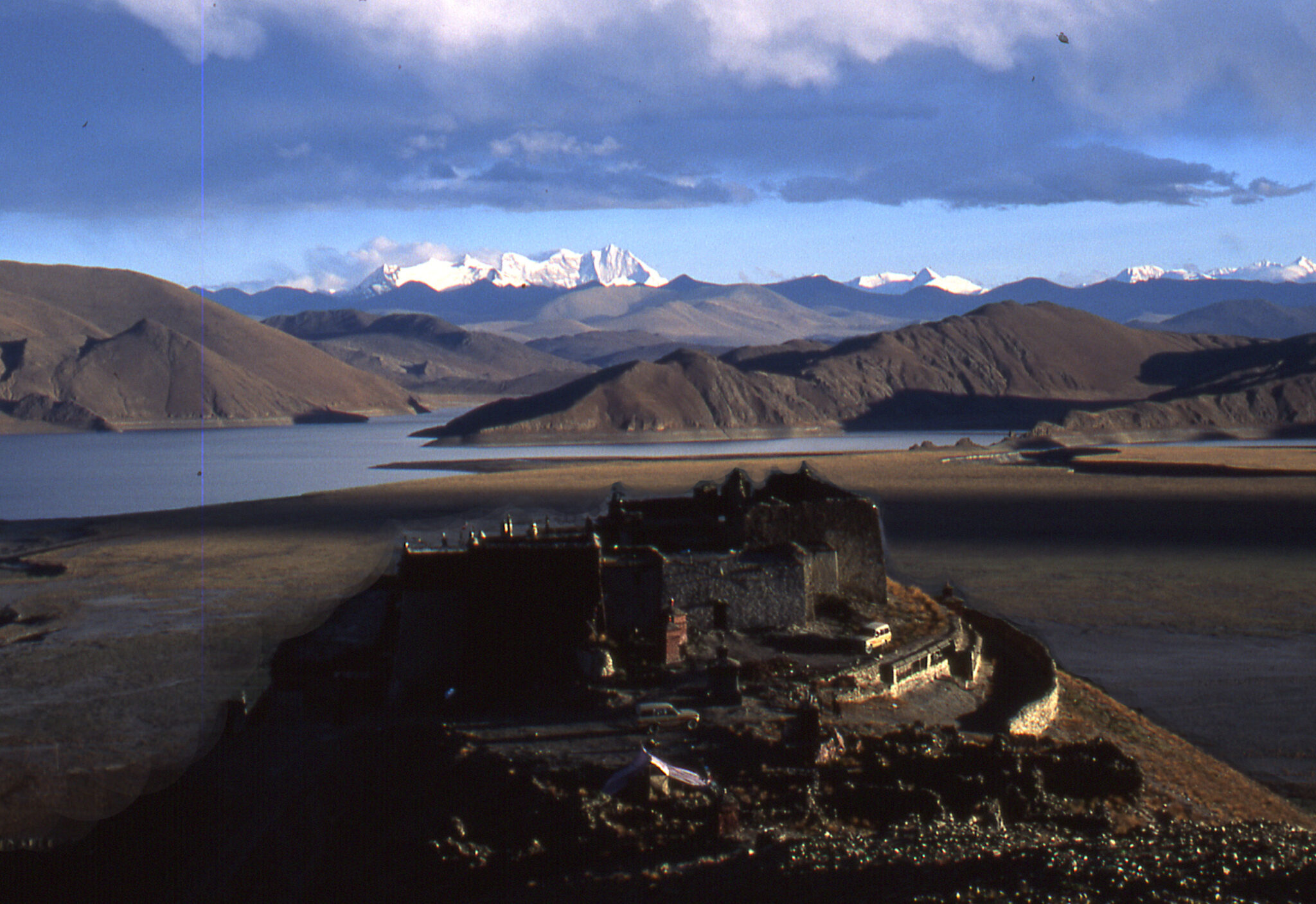 Hilltop monastery in foreground stands before sinuous lake and imposing, snowcapped mountain range in background