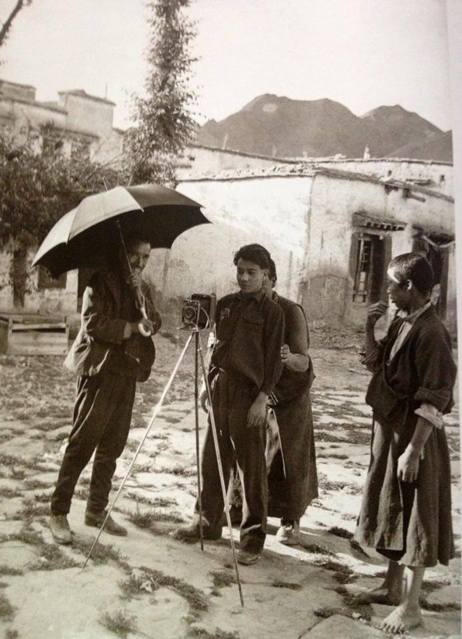 Black and white photograph of four people, one with umbrella, gathering around camera on tripod