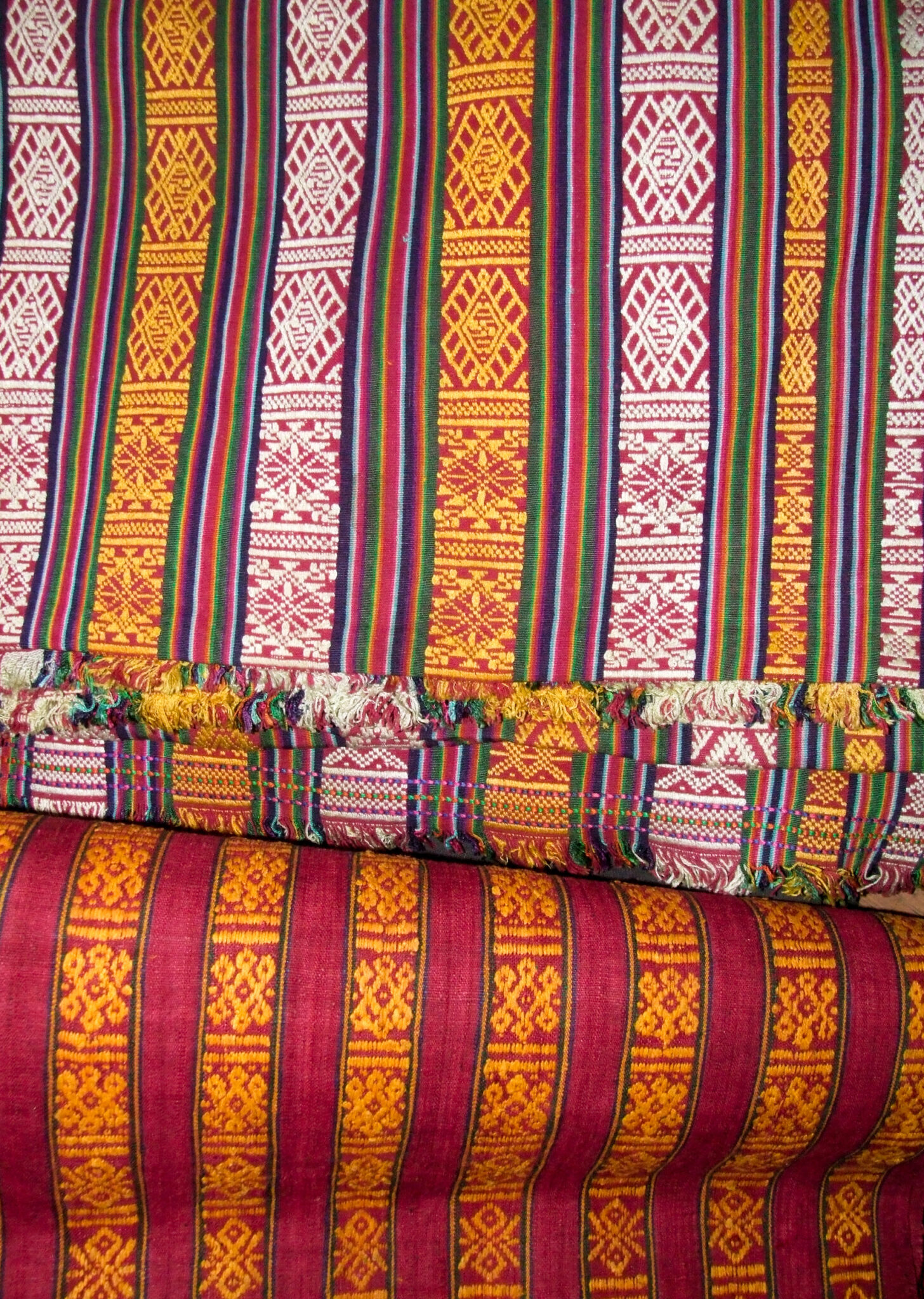 Two lengths of textile featuring vertical stripes decorated with geometric forms: Purple, white, and gold at top; Red and gold at bottom