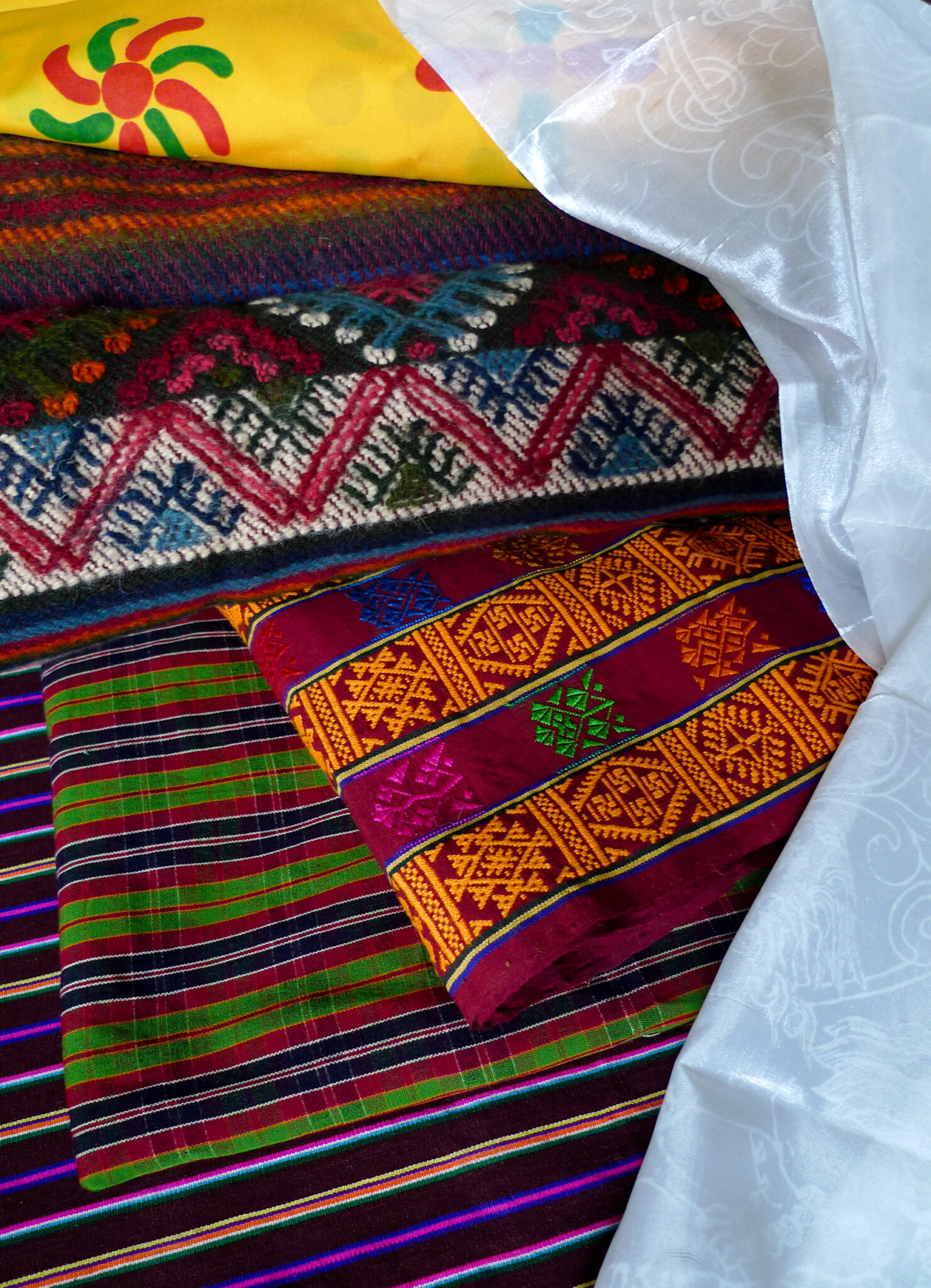 Five different types of textiles in multitude of colors displayed atop one another, all wrapped in white shawl