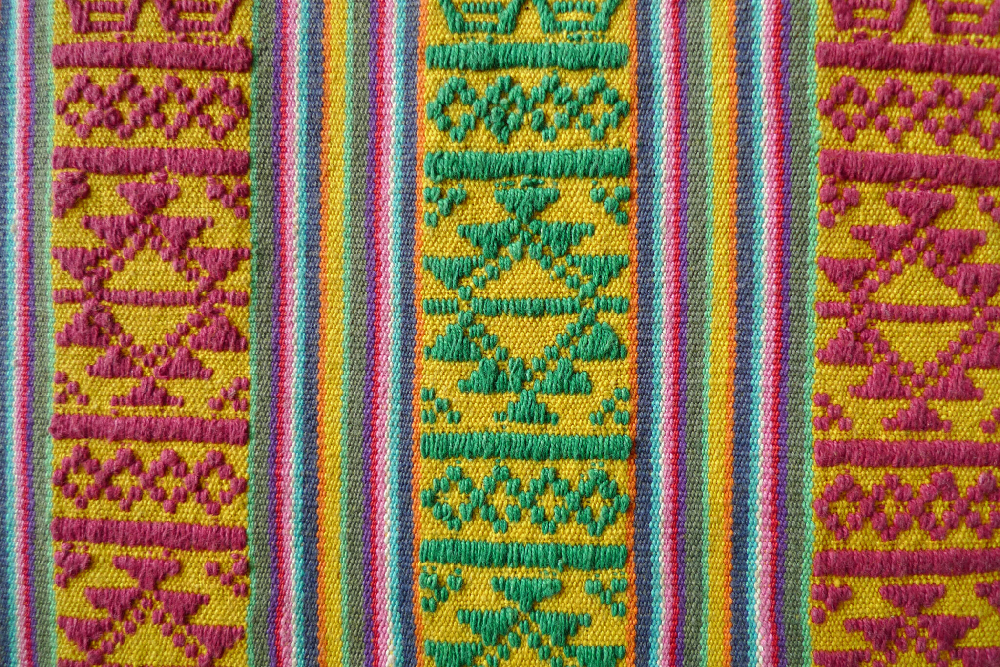 Detail of textile featuring vertical bands woven with geometrical patterns in yellow, green, red, and pink