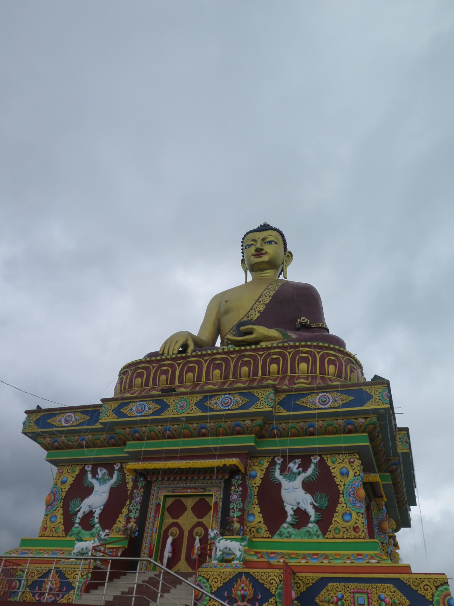 View from below of colossal Buddha statue seated atop colorful, magnificently decorated plinth