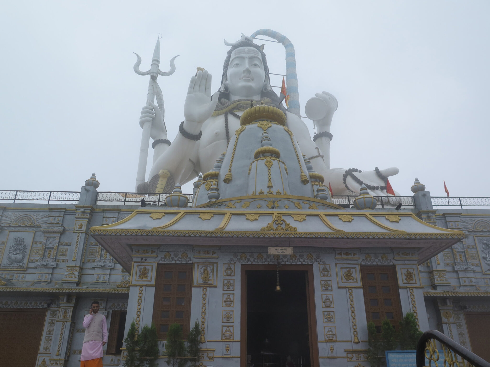 Colossal statue depicting Hindu deity towers above elaborately decorated gold and white entrance to plinth