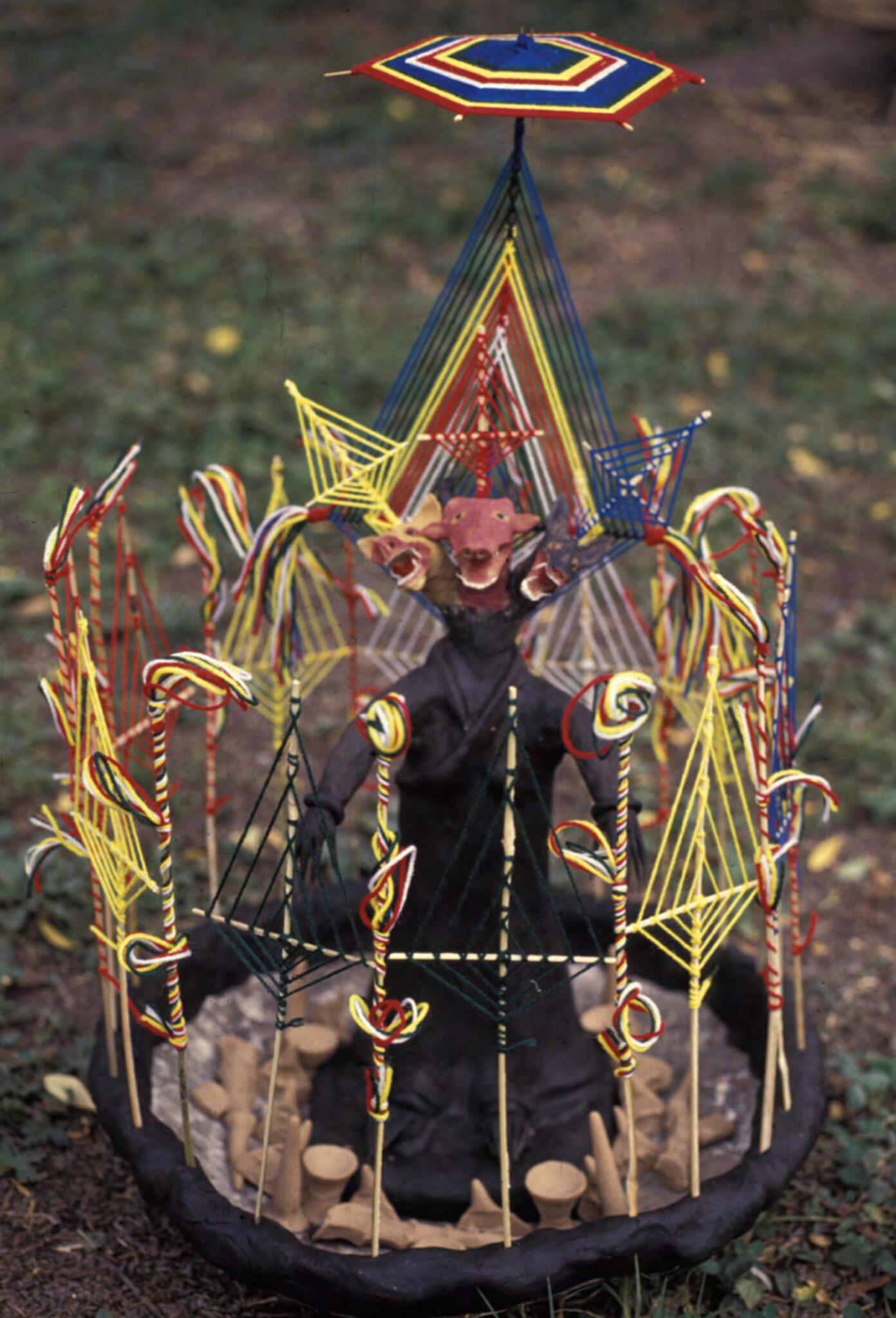 Effigy of three-headed figure surrounded and ornamented by woven lozenges in red, yellow, and blue