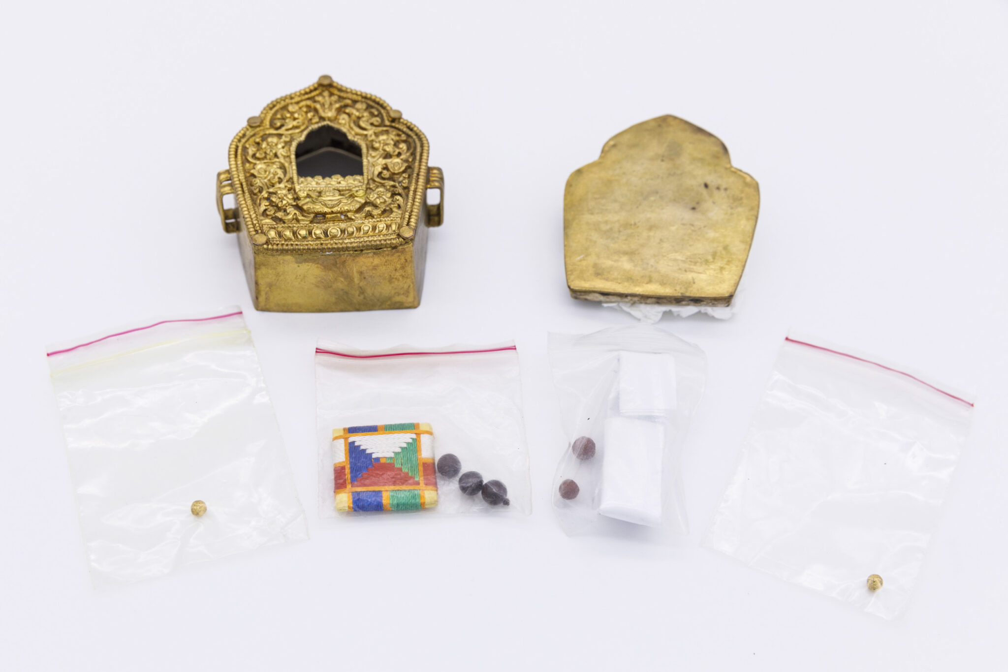 Golden nimbus-shaped box decorated with scrollwork; contents (beads, colorful square) displayed in plastic baggies