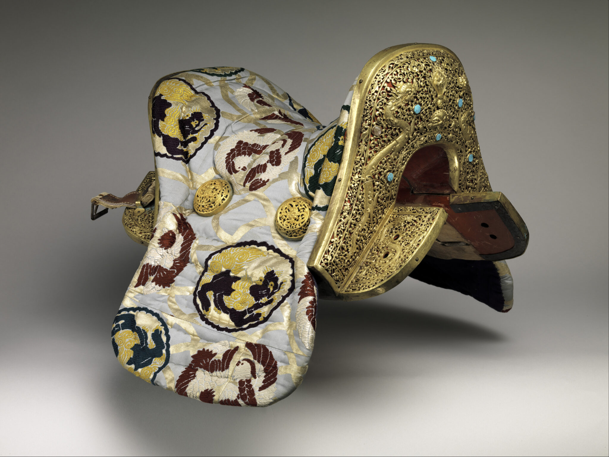 Golden filigreed saddle featuring turquoise insets; upholstered in blue, yellow, and red roundel-pattern textile