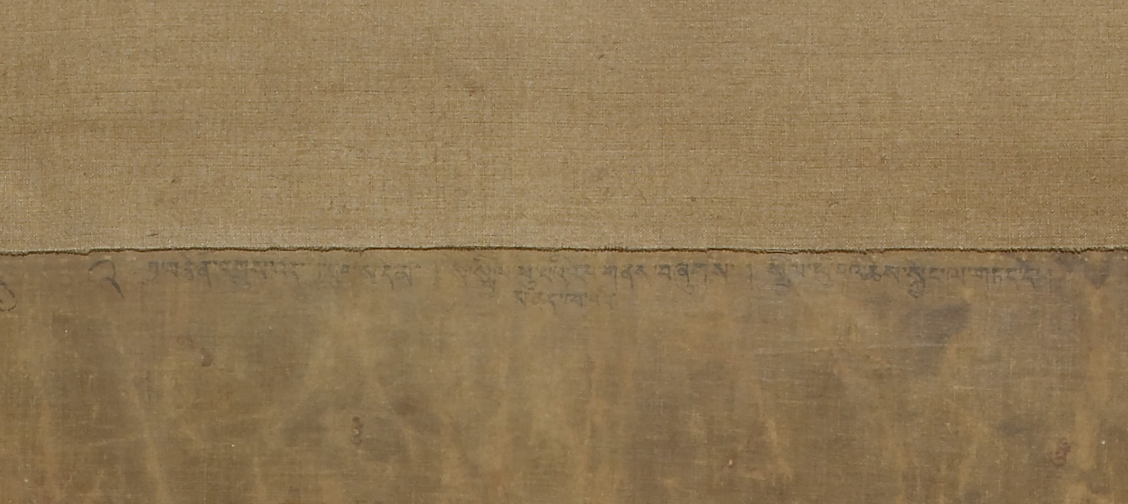 Close view of beige, textured surface with long line of Tibetan script at center underneath horizontal seam