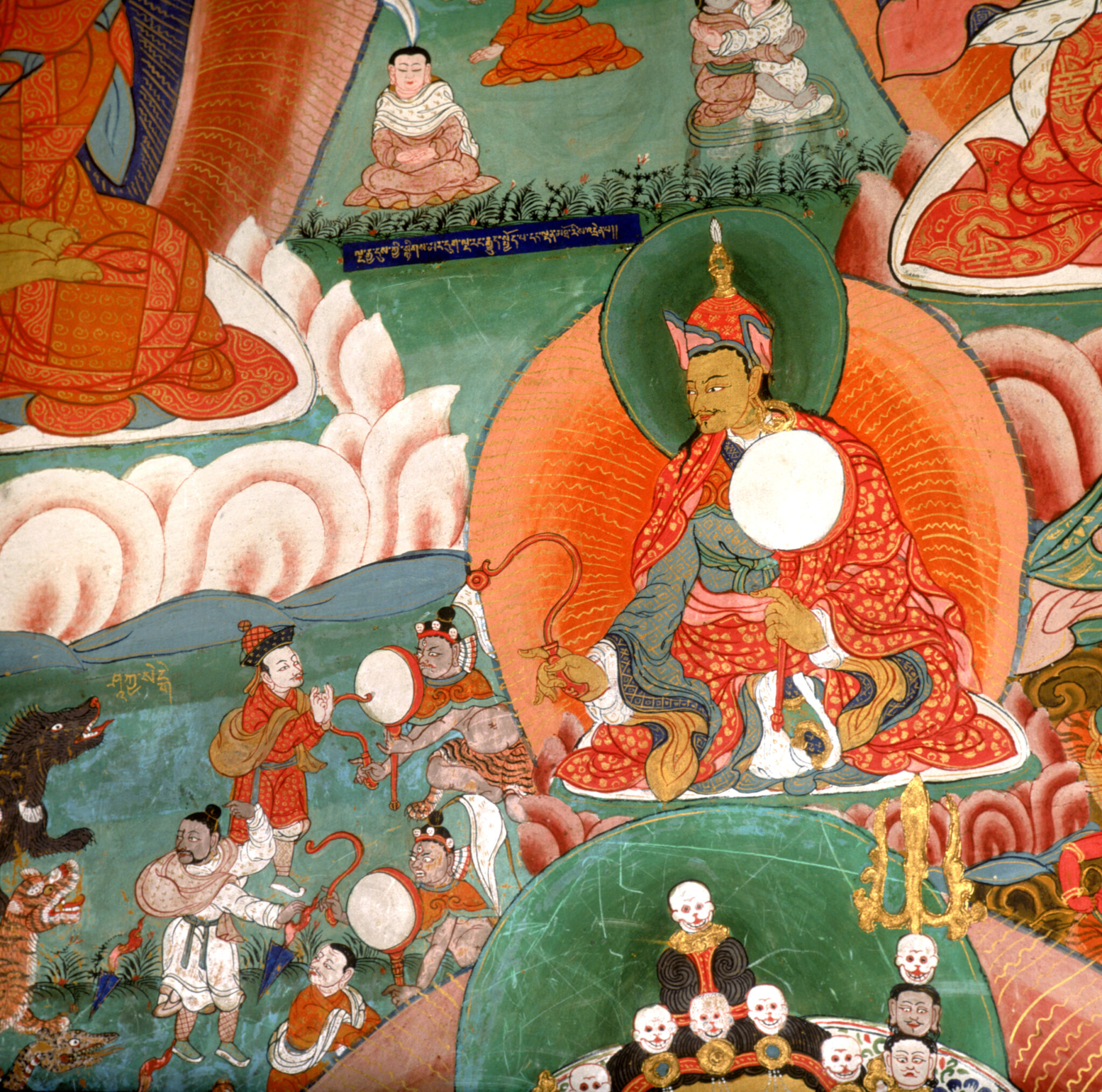 Guru wearing gold and red brocade robe and his attendants ward off animals attacking from left