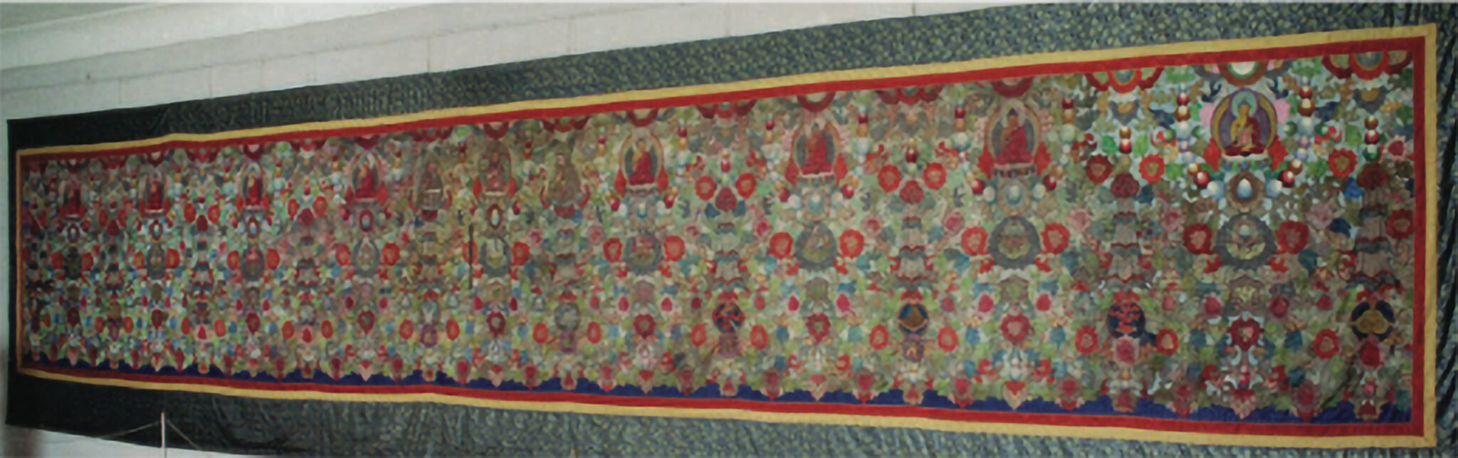 Long, wide embroidered textile in greens and reds mounted on green and gold brocade border