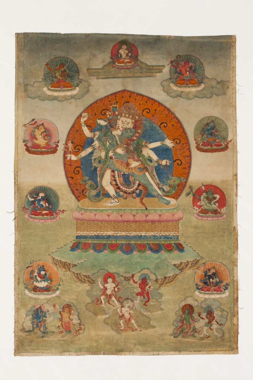 Six-armed deity stands in embrace with blue-skinned consort surrounded by deity portraits above sparse landscape