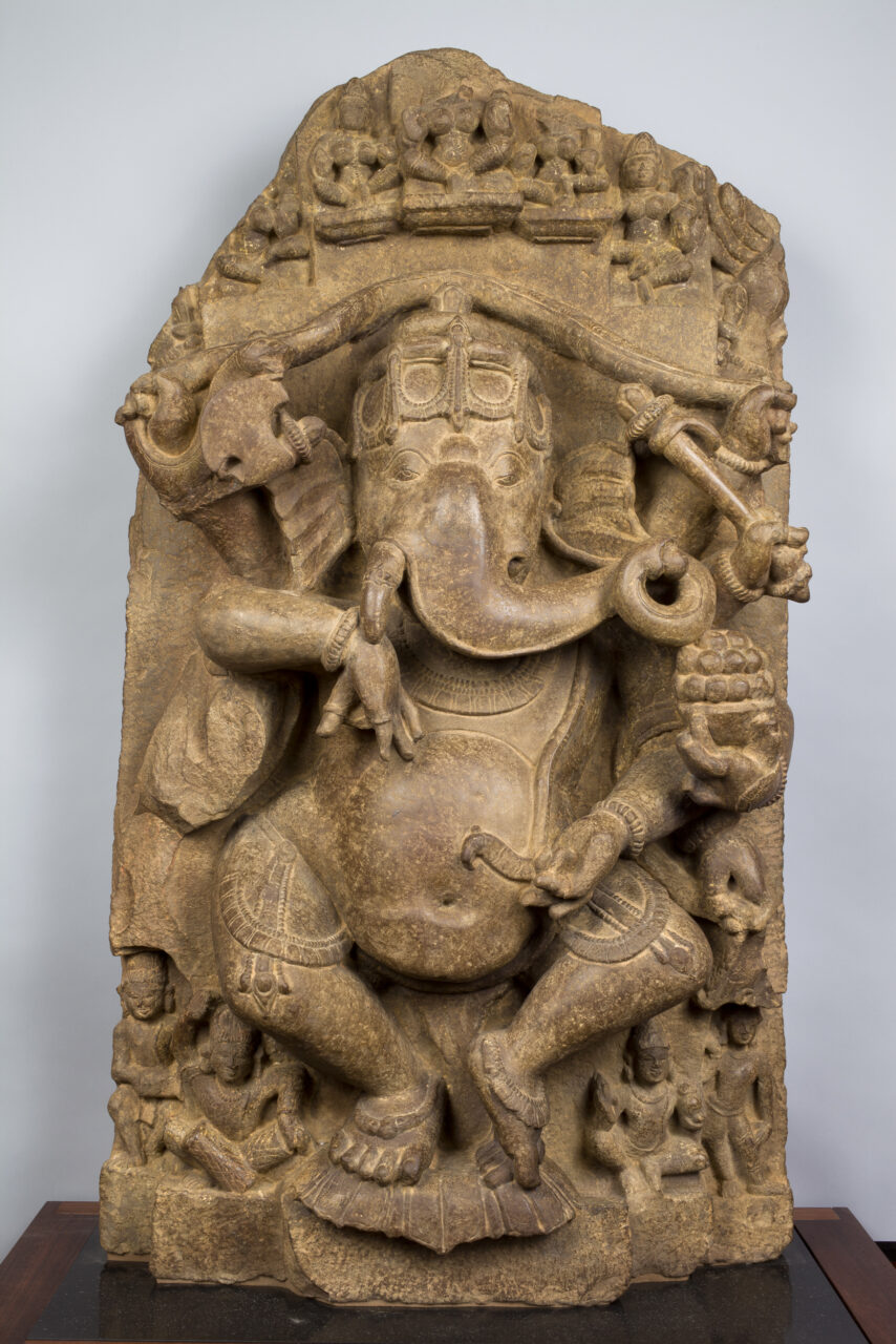 Sandstone relief sculpture depicting elephant-headed god dancing and holding implements in multiple hands