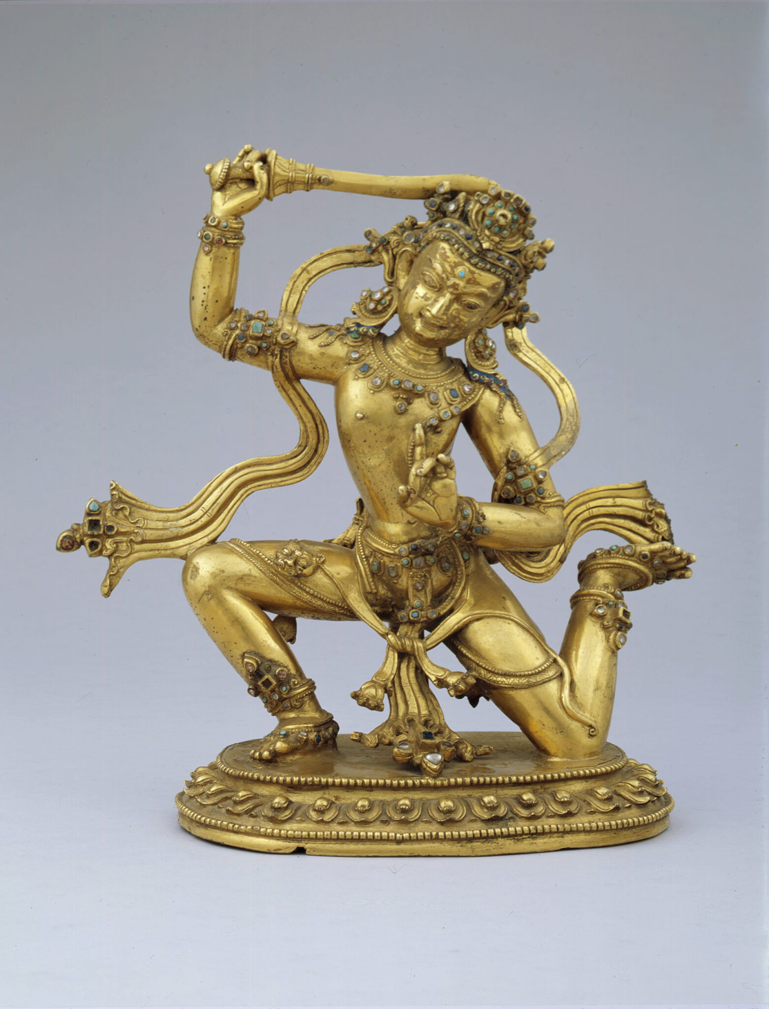 Golden statuette of kneeling deity with right foot upturned and sword held aloft in left hand, sash flowing about shoulders