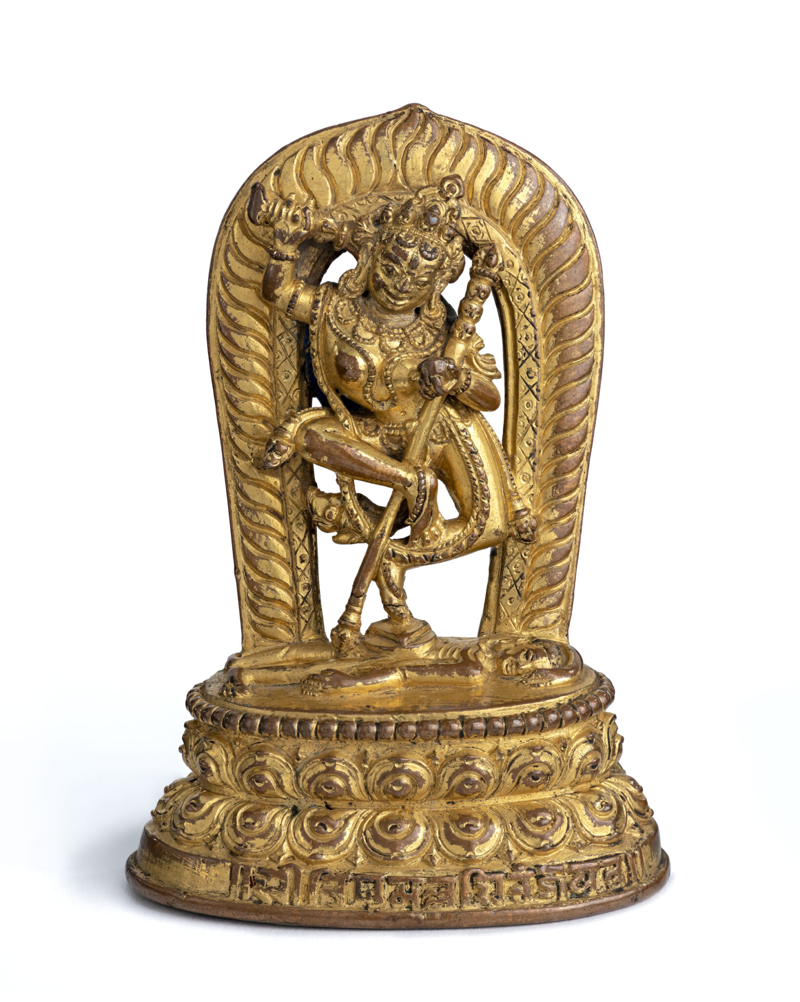 Gilded sculpture featuring dynamically posed deity standing atop supine figure before open fiery nimbus