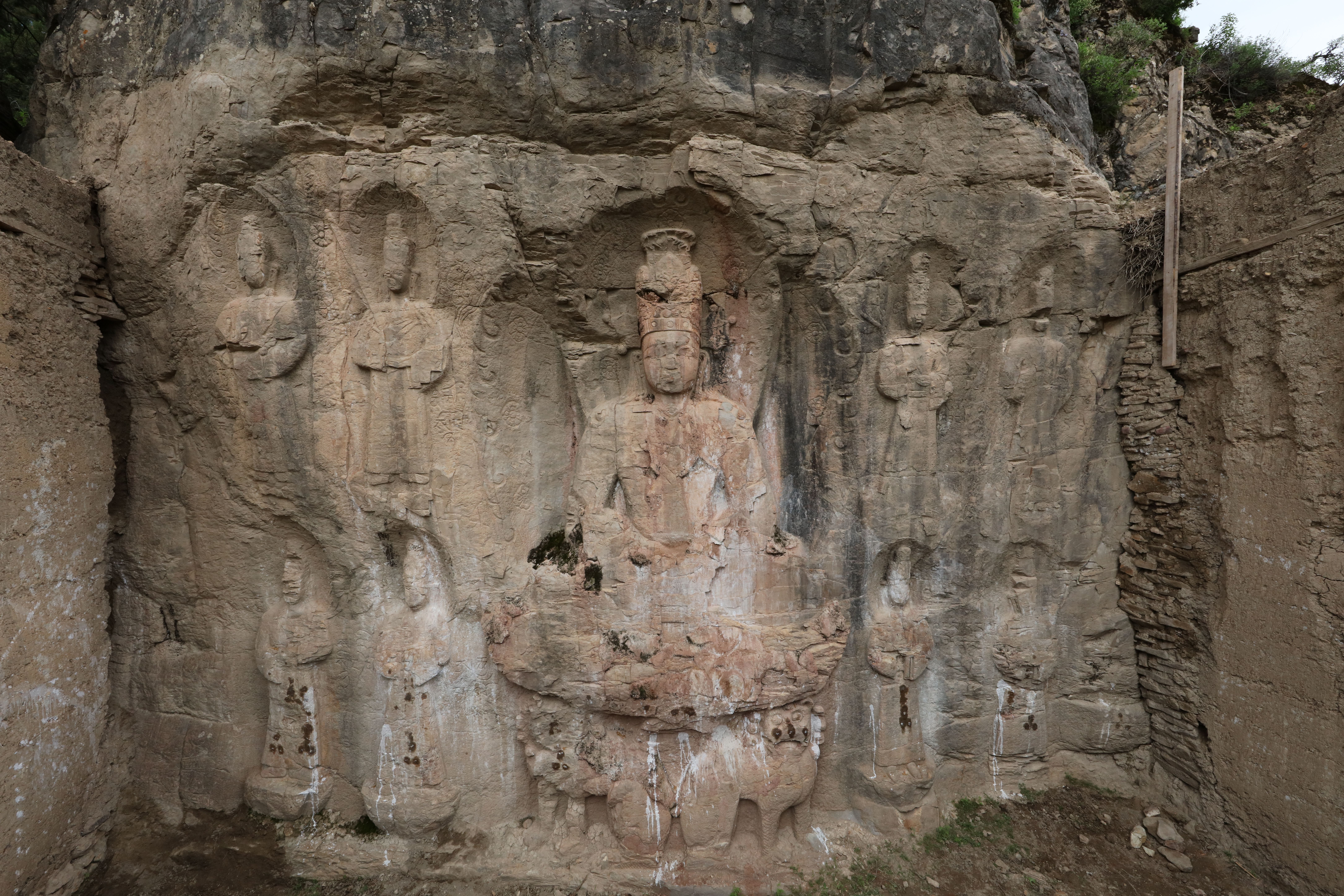 Wide view of monumental stone relief carved into excavated base of large rock